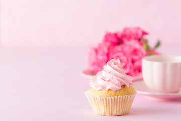 Cupcake with pink cream decoration and roses on pink pastel background.