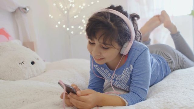 Cute little girl listening music with headphones and smart phone, 4k
