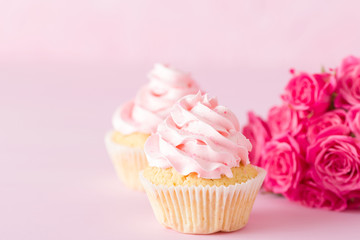Cupcake with pink cream decoration and roses on pink pastel background.
