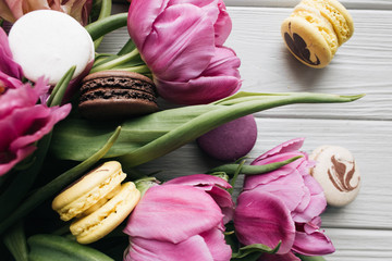 Delicious colorful macaroons and pink tulips on white wooden table, sweet dessert