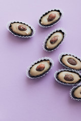 Composition of delicious praline sweets with almonds on purple background