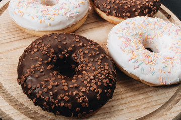 Sweet homemade donuts with sugar sprinkles and chocolate glaze on wooden board