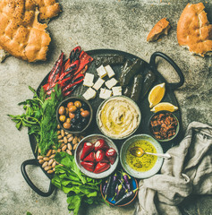 Mediterranean, Middle Eastern meze starters platter. Flat-lay of stuffed pickled paprikas, cheese, dolma, hummus, spiced oil, olives, sundried tomatoes, nuts, flatbread on tray, top view copy space