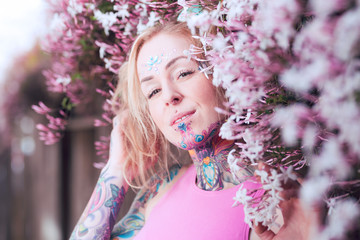 Tight portrait of blonde caucasian woman with tattoos near pink flowers