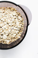 Raw oatmeal flakes in bowl on white background, healthy breakfast