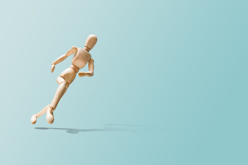 Wooden model on the run. Wooden mannequin in a running pose. Morning running, training. Jogging. The figure of wood runs on a pastel blue background. Concept of caring for physical condition.