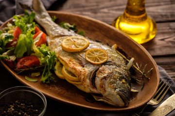 Grilled Dorado with lemon, thyme, rosemary and fresh salad on the wooden table.