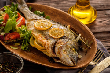 Grilled Dorado with lemon, thyme, rosemary and fresh salad on the wooden table.