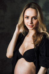 Fototapeta premium Close-up portrait of a beautiful pregnant woman with cute smile and blonde hair in black lingerie