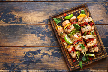 Grilled chicken kebab (skewers) with vegetables on a cutting wooden board.Top view with copy space.