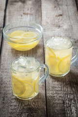 Two cups of lemonade and ice cubes crumbs on a wooden table background