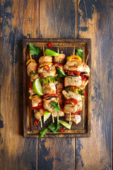 Grilled chicken kebab (skewers) with vegetables on a cutting wooden board.Top view with copy space.