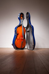 A antique cello stands inside a blue hard shell travel case ready for a musician to pack up and head to the orchestra.