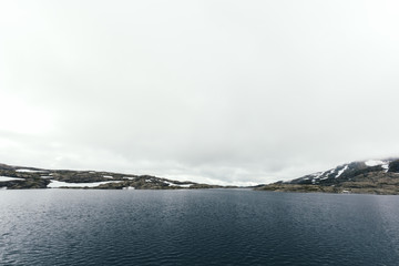 Typical norwegian landscape with snowy mountains and clear lake near the famous Trolltunga rock, Norway.