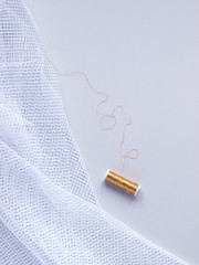 Single gold decorative string next to white net fabric on light gray background. Copy space. Flat lay. Top view