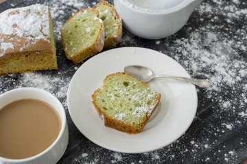 Mint cake sprinkled with powdered sugar on dark surface with cup of coffee