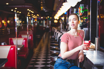 Young slim beautiful girl sits on a high bar stool in a cafe with stunning panoramic views of Barcelona. Siesta break with a cup of fragrant cappuccino