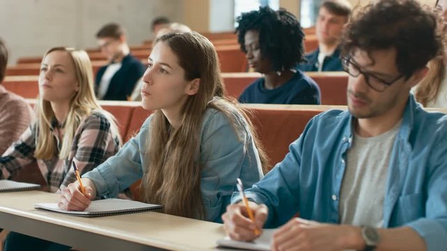 Group of Multi Ethnic Students in Classroom Listening to a Lecture and Taking Notes. Bright Young People Study at University. Shot on RED EPIC-W 8K Helium Cinema Camera.