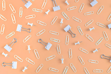 Stationery is chaotically scattered on a orange background. White paper clips and clerical buttons are in a mess. Beautiful picture from the top.