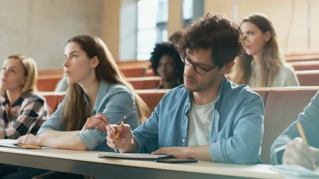 Hispanic Young Man Among His Fellow Students in the Classroom. Young Bright People Listening to a Lecture and Take Notes while Studying at the University. Shot on RED EPIC-W 8K Helium Cinema Camera.
