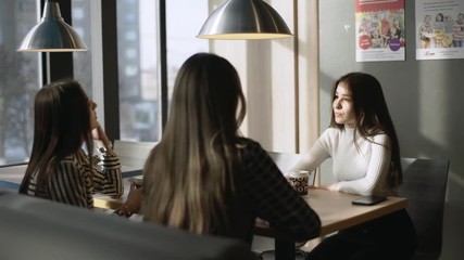 Friends in a cafe bar. Girls drink coffee in a cafe. Three girlfriends are sitting at a table in a cafe.