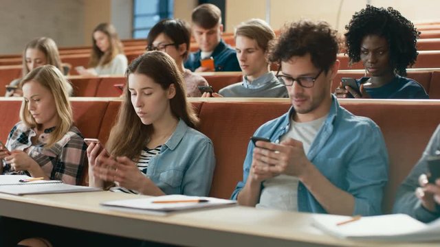 Multi Ethnic Group of Students Using Smartphones During the Lecture. Young People Using Social Media while Studying in the University. Shot on RED EPIC-W 8K Helium Cinema Camera.