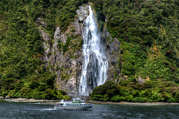 Fototapeta na wymiar Cruise ferry and beautiful high waterfall in Milford Sound, Fiordland National park, New Zealand
