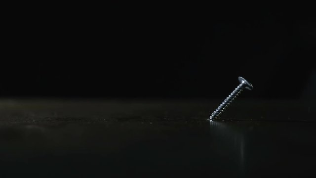 Screw is on a dark background. Hammer hits the screw, it bends. Close up. Concept: means does not correspond to the purpose, unreasonable use of force, force is-mind is not necessary, a waste of time