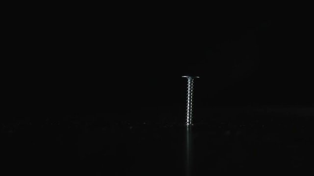Screw is on a dark background. Hammer hits the screw, it remains in place. Close up. Concept: means does not correspond to the purpose, unreasonable use of force, force is-mind is not necessary, a