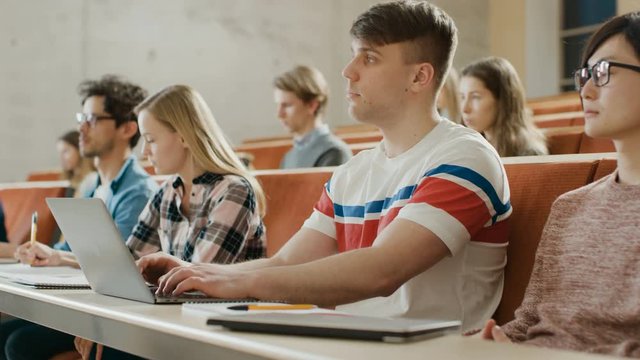 Handsome Caucasian Student Uses Laptop while Listening to a Lecture at the University. Shot on RED EPIC-W 8K Helium Cinema Camera.