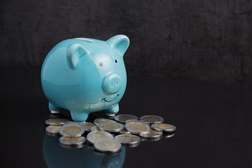 Money savings with blue piggy bank on dark black table with coins using as finance or investment concept