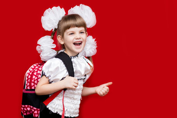 Cute smiling little girl in school uniform and white bows with backpack on red background. Back to school. Education and school concept