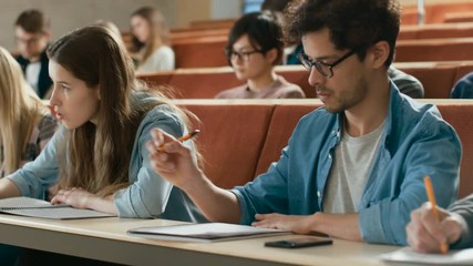 In the Classroom Multi Ethnic Students Listening to a Lecturer and Writing in Notebooks. Smart Young People Study at the College. Shot on RED EPIC-W 8K Helium Cinema Camera. - Powered by Adobe