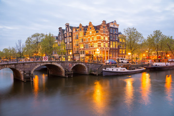 Fototapeta na wymiar Amsterdam canal, bridge and typical houses, boats and bicycles during evening