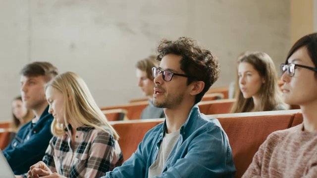 Handsome Hispanic Student Uses Laptop while Listening to a Lecture at the University, He Raises Hand and Asks Lecturer a Question. Shot on RED EPIC-W 8K Helium Cinema Camera.