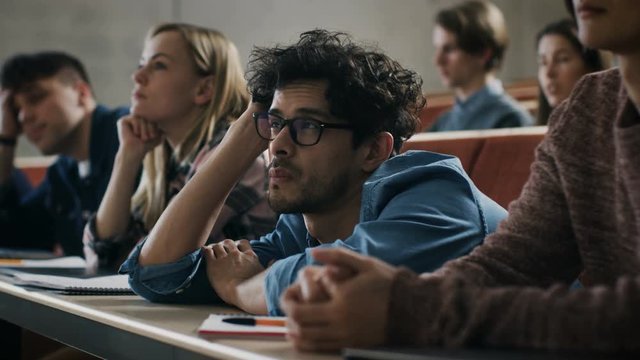 Bored Male Student Listens Lecture at the University. Tired, Exhausted and Overworked Young Male Holds His Head. Shot on RED EPIC-W 8K Helium Cinema Camera.