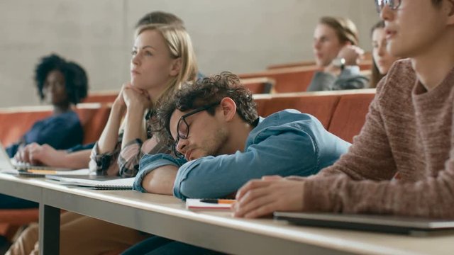 Tired Male Student Sleeps on a Lecture at the University. Exhausted and Overworked Young Male.  Shot on RED EPIC-W 8K Helium Cinema Camera.