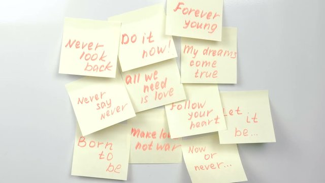 Motivation phrases on yellow sticker paper sheets on a white board.