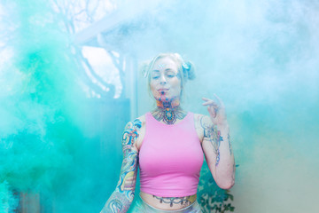 Obraz na płótnie Canvas Wide portrait of blonde caucasian woman with tattoos using green smoke bomb in an urban location