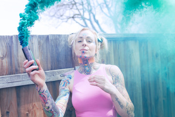 Wide portrait of blonde caucasian woman with tattoos using green smoke bomb in an urban location