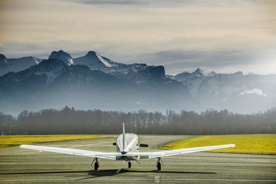 Fototapeta Propeller plane parking at the airport. Small airfield in front of high mountains. Sunset over mountains.