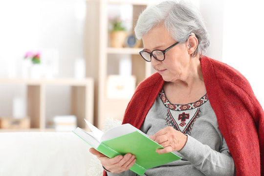 Mature woman with hearing aid reading book indoors