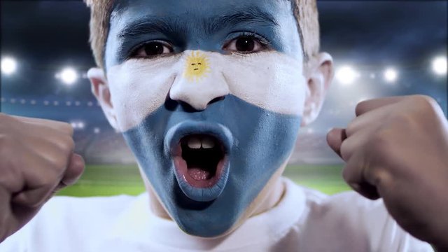 Boy yelling goal with his face painted with the Argentina flag and stadium on the background