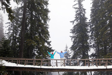 Happy couple standing on bridge in snowy forest. Winter vacation