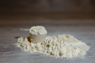Close-up scoop in protein powder slides on a wooden table. bunch of protein powder with plastic spoon on white background. Dry mixture for dilution with milk or water. Sports dietary nutrition.