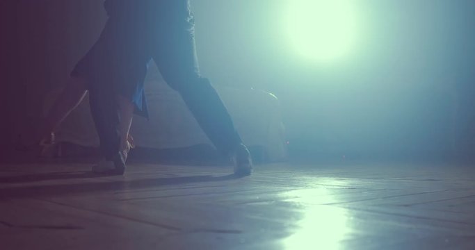 Legs of couple learning to dance tango in the studio. Close up. Silhouette