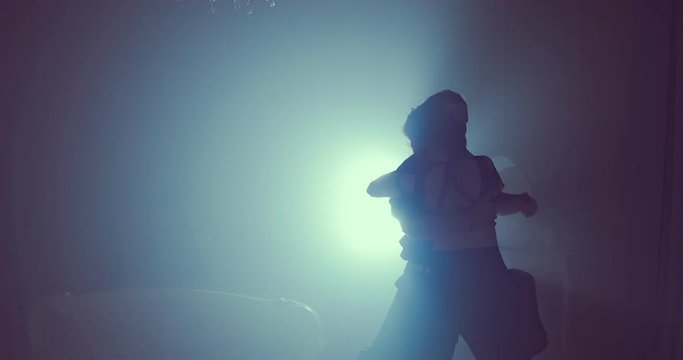 Woman and man are pressed against each other and dancing in ballroom. Slow motion. Silhouette