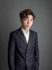 Portrait of a smart young Chinese man standing against gray background, looking at camera with confidence expression.