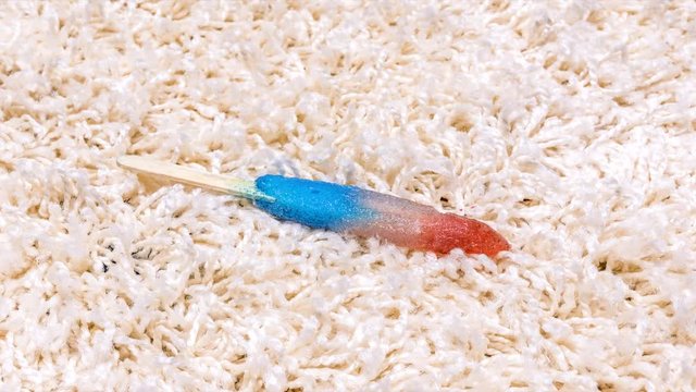 A time lapse of a melted popsicle reforming its icy structure on white carpet.