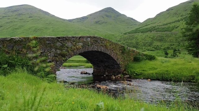 Views of Butterbridge crossing Kinglas Water, the old small arch bridge near Loch Lomond National Park, Scotland. Mountain river flows through the green valley. Steady shot and panning close-up scenes